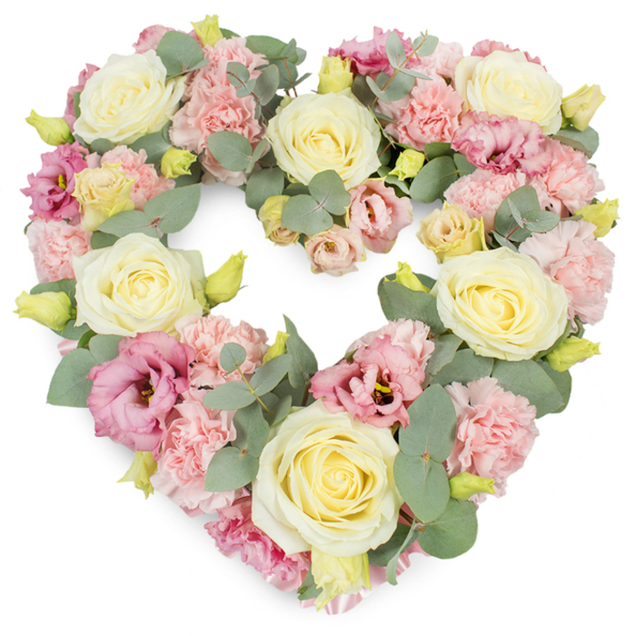 A softly coloured, heart-shaped wreath of sympathy flowers fills the frame, carefully arranged against a clean white backdrop to emphasise every petal and leaf-a design that would feel at home in a peaceful Enfield Town service or chapel. The heart itself is full and well-rounded, with no bare patches, giving it a luxurious, cushioned appearance. Cream and pale yellow roses form the main anchors of the piece, their velvety petals spiralling in tight, elegant whorls that gradually open out, suggesting tenderness and enduring devotion. Nestled between them, clusters of pastel pink carnations bring a charmingly ruffled texture; each bloom consists of many small, frilled petals that overlap like fine lace. Scattered among the softer hues are lisianthus (eustoma) blossoms in deeper pink and mauve, their slightly flared, cup-shaped petals introducing a measured richness and sophistication. Running throughout the arrangement are stems of eucalyptus with silvery-green, round leaves, adding cool tones and a gentle, natural structure that helps define the heart's contour-much like the calming greenery found in the quieter corners of Enfield Town. Small, tightly furled yellow-green buds are dotted through the design, hinting at fresh growth and newly cut stems, an understated symbol of continuity. The heart outline is clear, symmetric, and visually soothing, the result of careful, experienced floristry. This floral tribute speaks of love, remembrance, and sympathy, making it fitting for funerals, memorials, or anniversaries where families wish to send a message of comfort and respect. The overall impression is one of serene beauty and heartfelt care, conveyed entirely through flowers.